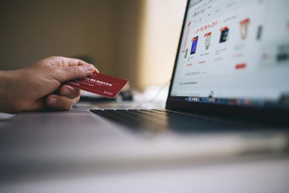 A hand holding a payment card in front of a laptop showing an online store