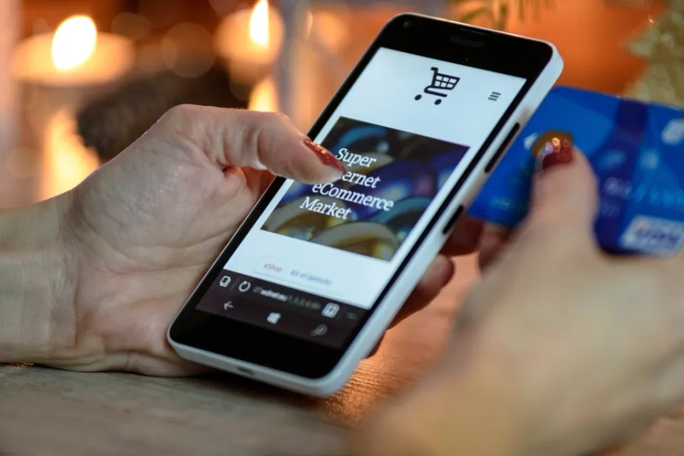 A shopper holding a phone showing an online store, with a payment card in the other hand