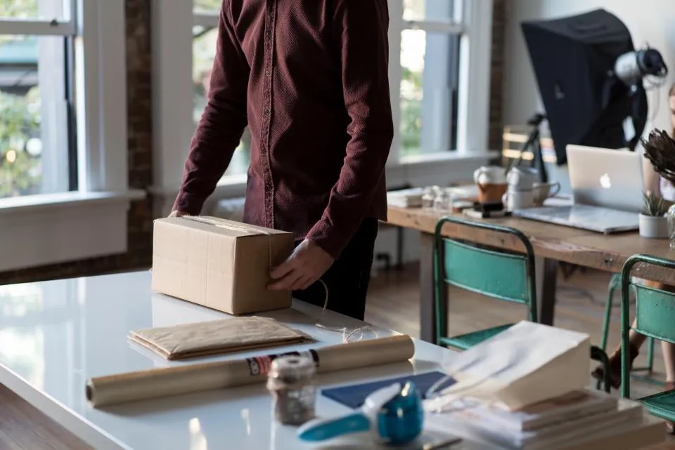 A person packing an order into a cardboard box at a workbench