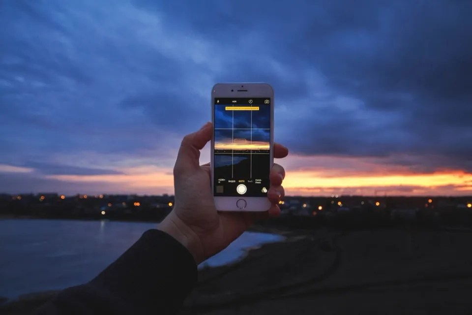 A hand holding up a phone to film a sunset